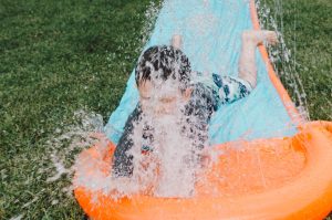 child sliding on blue and orange slippery pad with water splash at daytime